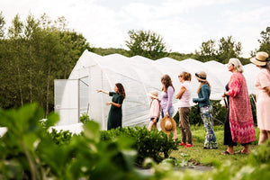 Un groupe de personnes suit une visite guidée autour d’une serre transparente, entourée de verdure et de champs en pleine nature.